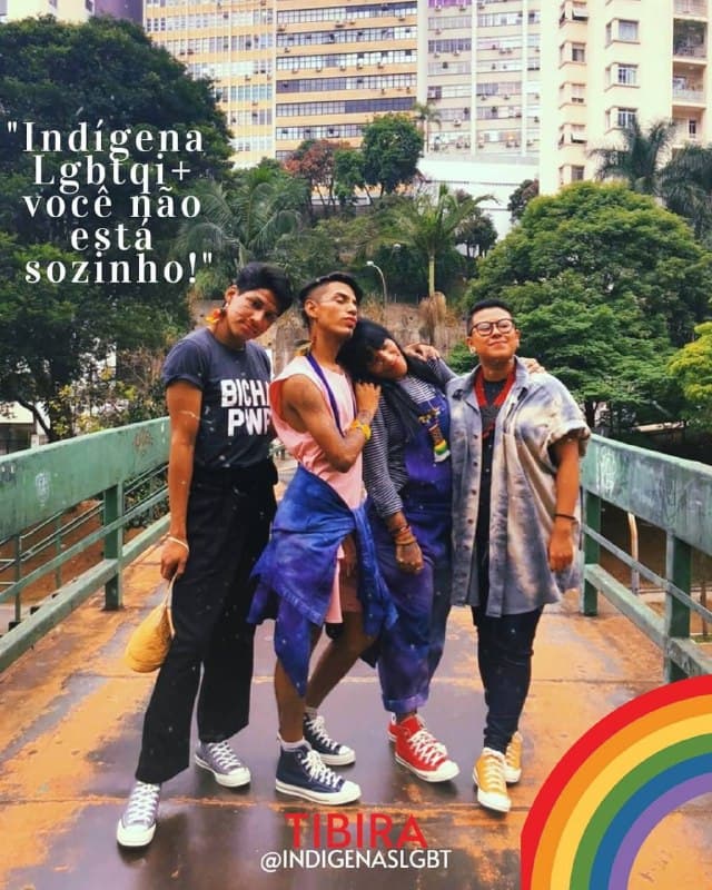 Grupo de pessoas indígenas LGBTQIA+ em uma passarela, com a bandeira do arco-íris