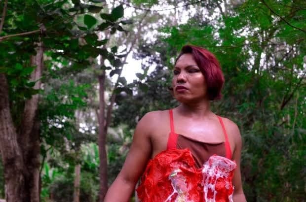 Majur, cacique trans, em meio à mata, com cabelo curto vermelho e blusa vermelha