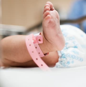 Pé de um bebê recém-nascido com pulseira de identificação rosa